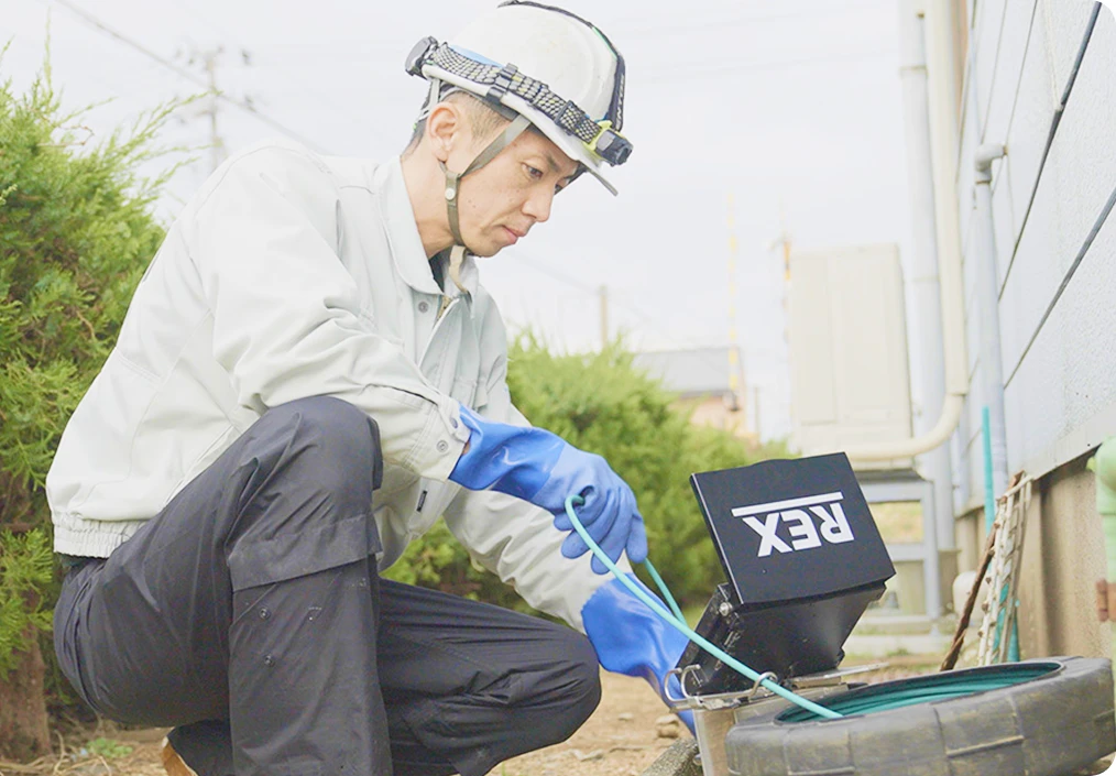 屋外で配管内を管内カメラで調査する社員の写真